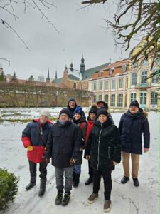 Uśmiechnięta grupa mężczyzn i kobiet stojąca zimą przed pałacem w Parku w Oliwie.